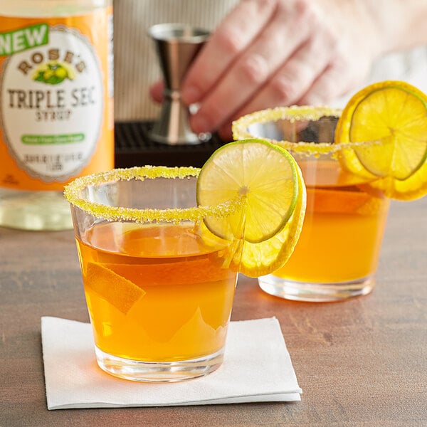 A hand holding a glass of Rose's Triple Sec with a sugar rim and a lime slice.