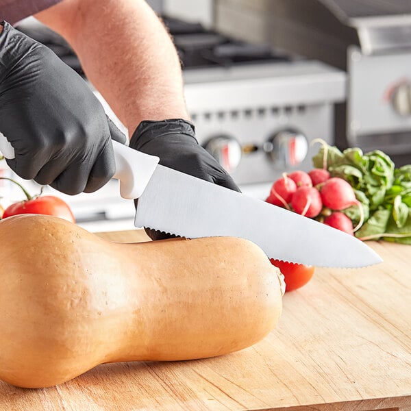 A person wearing black gloves using a Choice serrated chef knife to cut a butternut squash.