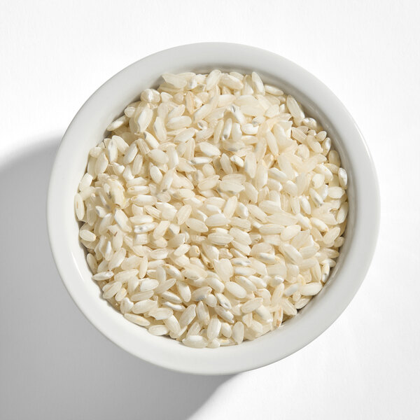 A white bowl filled with uncooked Carnaroli rice grains.