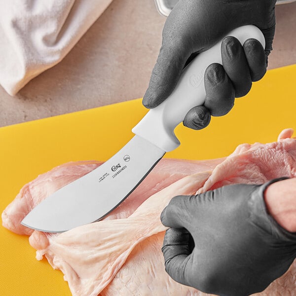 A person in gloves using a Choice curved skinning knife with a white handle to cut meat.