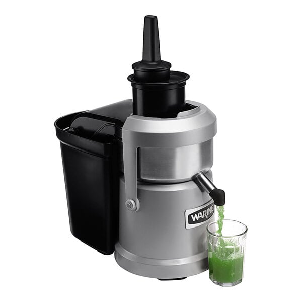 A Waring juice extractor pouring green juice into a glass.
