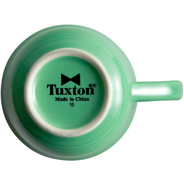 A close-up of a green Tuxton tea cup with a logo.