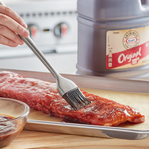 A person using a brush to apply Kraft BBQ sauce to meat.