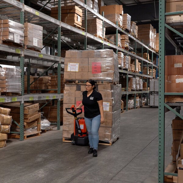 A woman in a black shirt and blue jeans pushing a Ballymore lithium battery powered pallet truck in a warehouse.