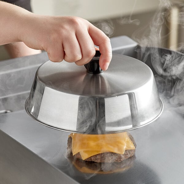 A hand holding a metal lid over a cheeseburger.