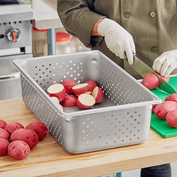 A woman cutting red potatoes in a Vollrath stainless steel steam table pan.