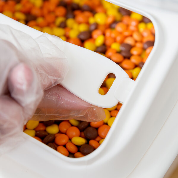 A person using a white plastic lid to cover a Baker's Mark ingredient bin filled with candy.