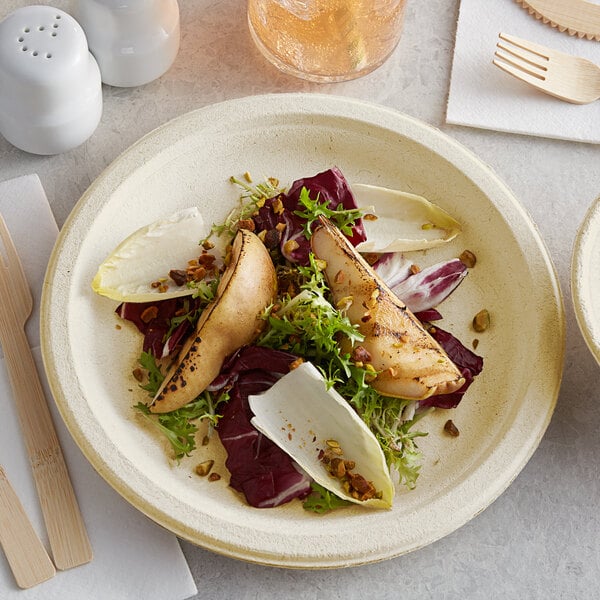 A Tellus natural bagasse plate with food including a salad and a wooden fork on a table.