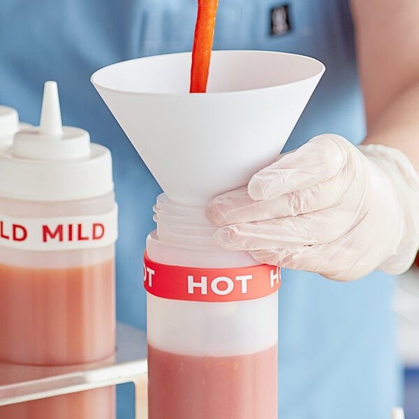 A hand using a red silicone band to pour hot liquid into a bottle.