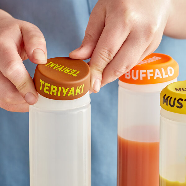 A hand using a white silicone lid to dispense sauce from a bottle.