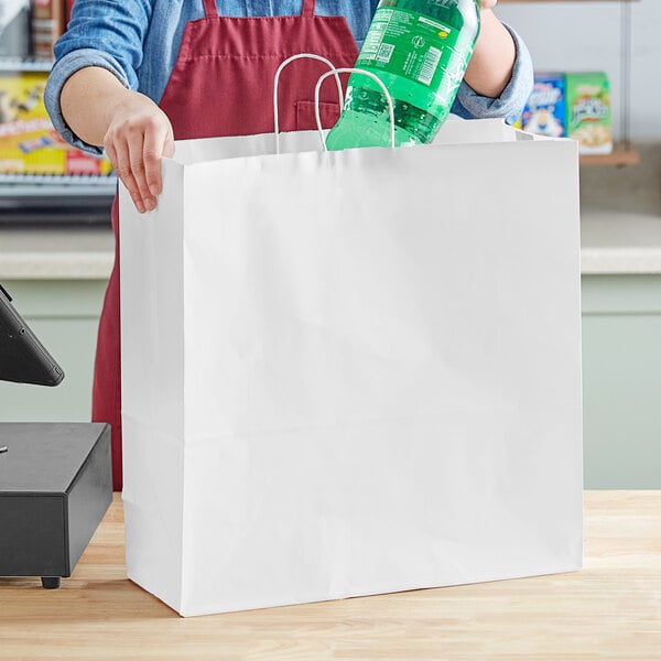 A woman putting a bottle of soda into a white paper shopping bag.