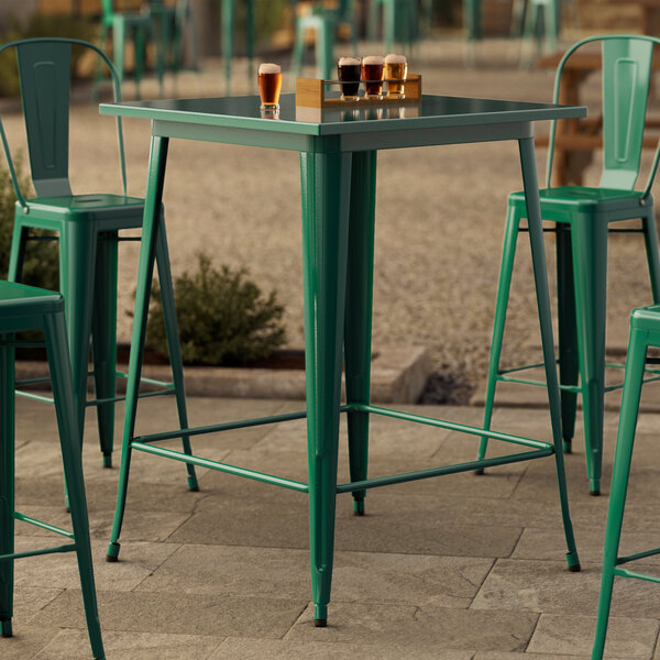 A Lancaster Table & Seating emerald green bar table on a stone surface.