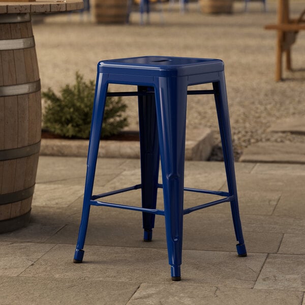 A blue Lancaster Table & Seating outdoor backless counter height stool sitting on a stone surface.