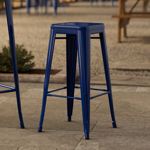Two blue Lancaster Table & Seating outdoor backless barstools on a stone patio.