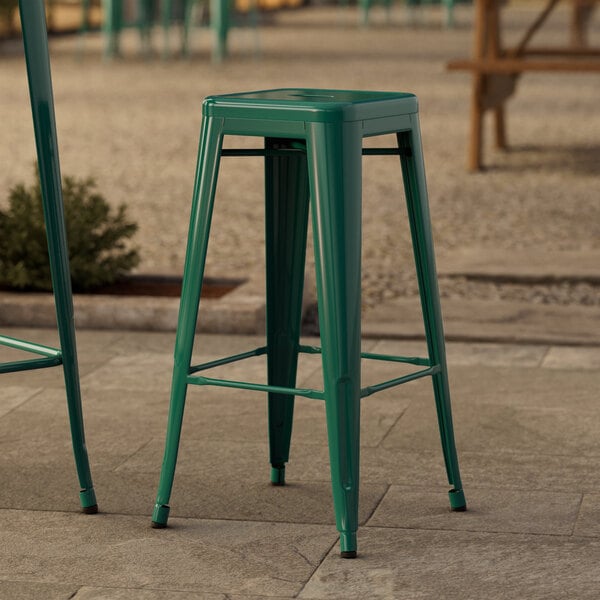 Two green Lancaster Table & Seating outdoor barstools on a stone patio.