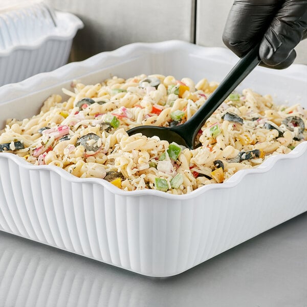 A person using a black spoon to serve food from a white Choice Deli Crock.