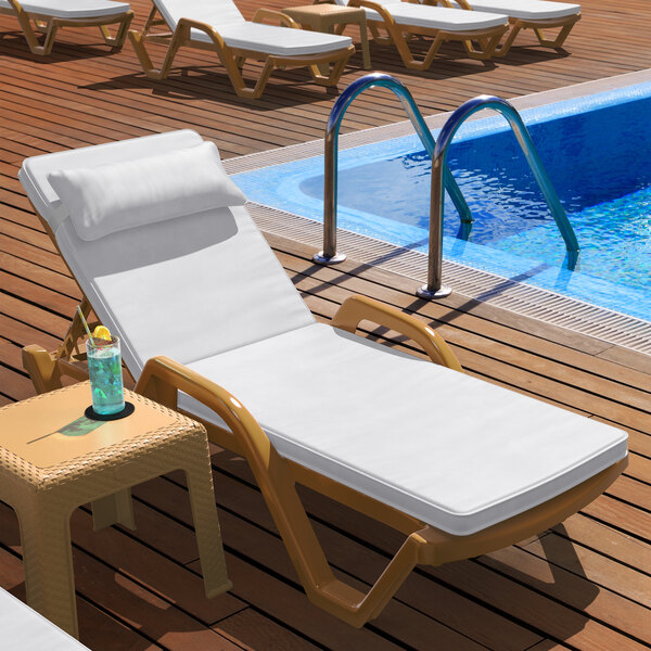 A Lancaster Table & Seating Sand resin chaise with white cushion and pillow next to a pool.