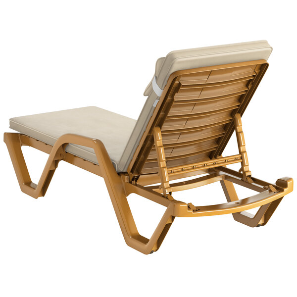 A Lancaster Table & Seating sand resin chaise lounge with cream cushion and pillow.