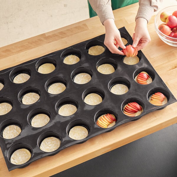 A person using a Sasa Demarle Flexipan Tatin tartlet mold to make apple tartlets.