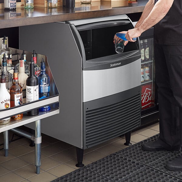 A man putting a glass of ice on a counter with a Scotsman undercounter ice machine.