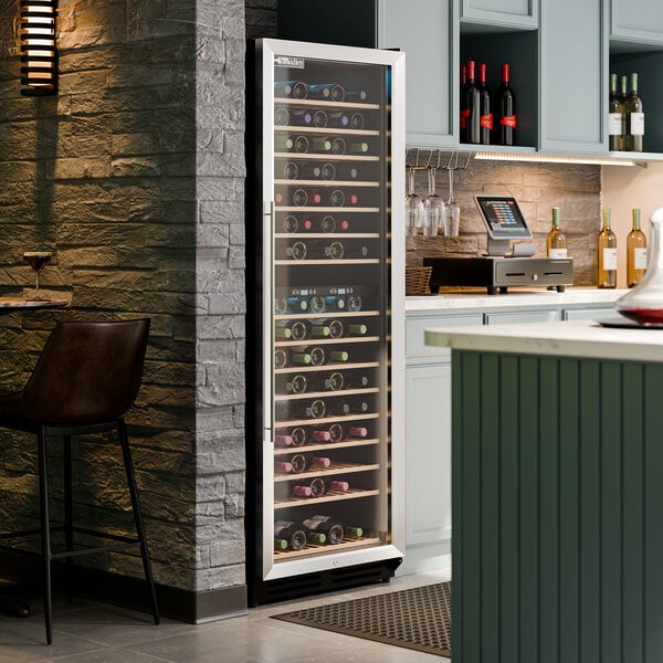A tall, glass-door commercial wine cooler filled with wine bottles, situated in a modern kitchen or bar area.