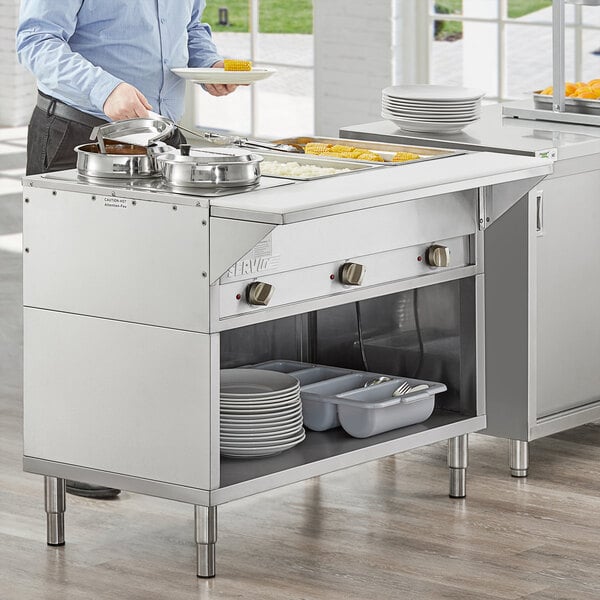 A man holding a plate of food in a school kitchen with a ServIt electric steam table on the counter.