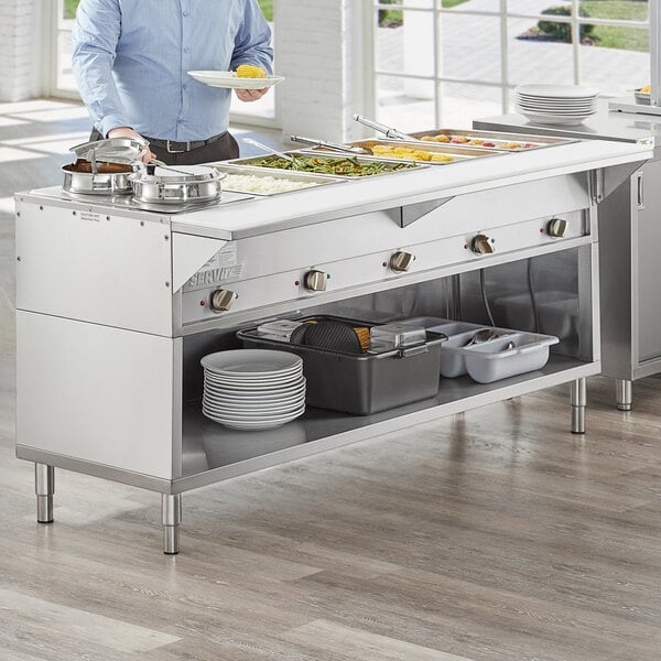 A man standing behind a ServIt open well electric steam table filled with food.