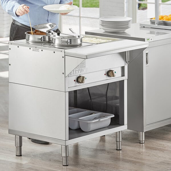 A woman using a ServIt electric steam table on a counter in a professional kitchen.