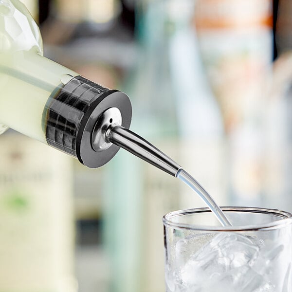 A bartender using a stainless steel liquor pourer to pour a drink into a glass.