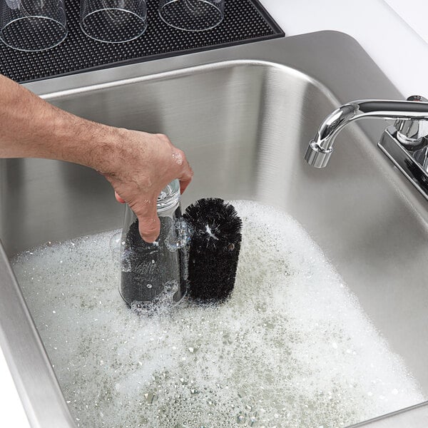 A person using a Bar Maid manual glass washer to clean a glass.