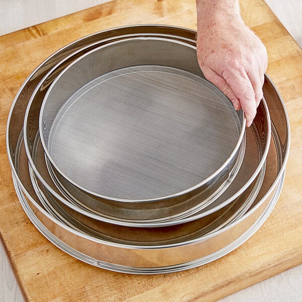 A hand holding a Choice 12" stainless steel sieve.