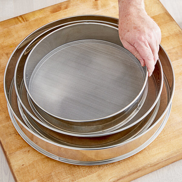 A hand holding a Choice stainless steel sieve.