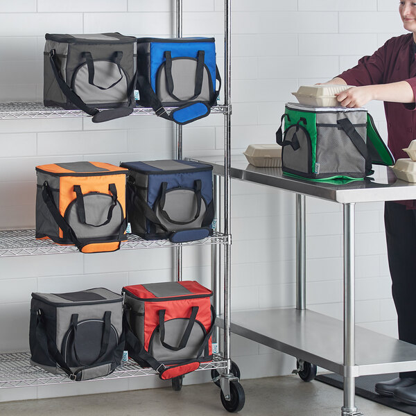 A woman standing next to a blue and grey Choice insulated cooler bag on a metal table with wheels.