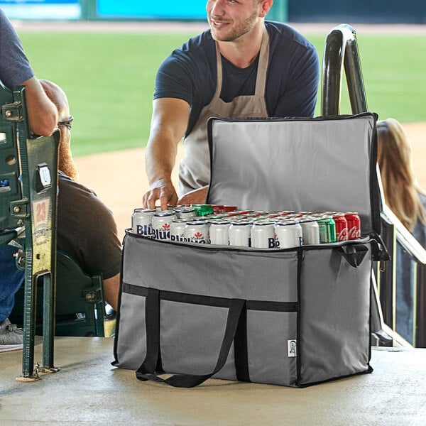 A man in an apron holding a gray Choice large insulated cooler bag filled with cans of beer.