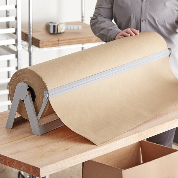 A person holding a Lavex Natural Kraft packing paper roll on a table.