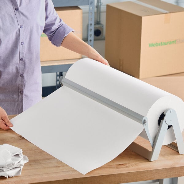 A large roll of white newsprint packing paper on a metal dispenser, being pulled by a person.
