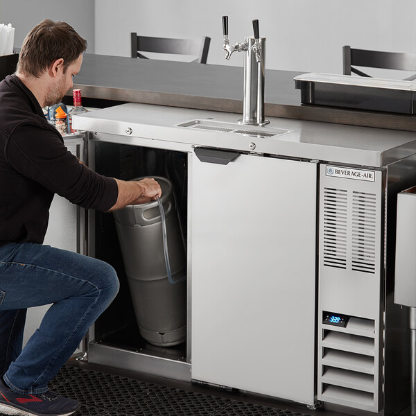 A man putting a wine keg into a Beverage-Air wine kegerator on a counter.