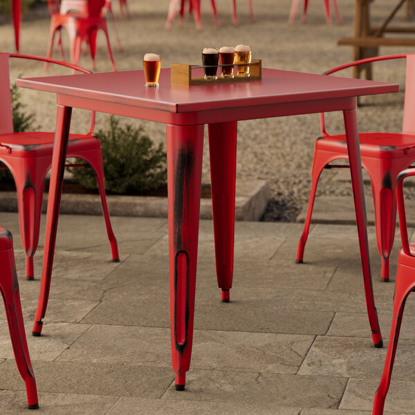 A Lancaster Table & Seating red table on a patio with glasses of beer on it.