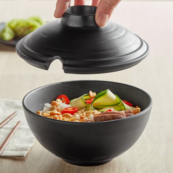 A person holding a black Nara melamine bowl with food inside.