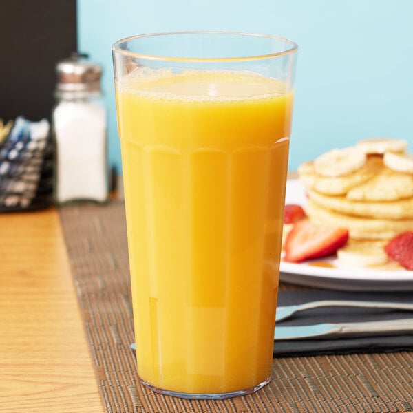 A Cambro clear plastic tumbler filled with orange juice on a table with pancakes.