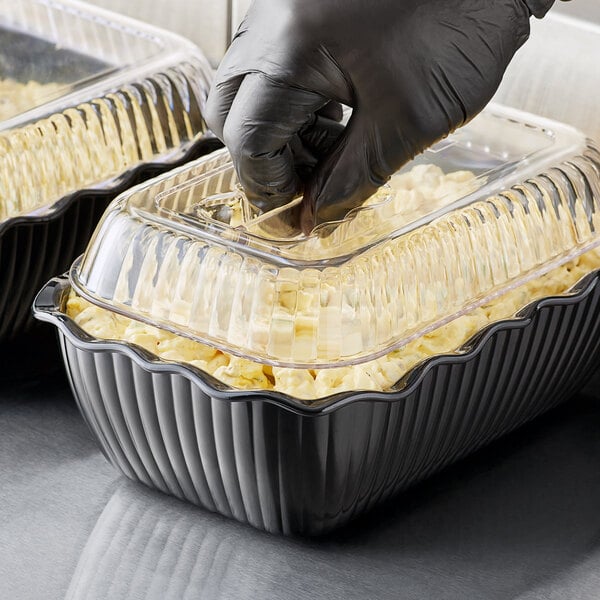 A person wearing black gloves putting food into a Choice black deli crock on a salad bar counter.