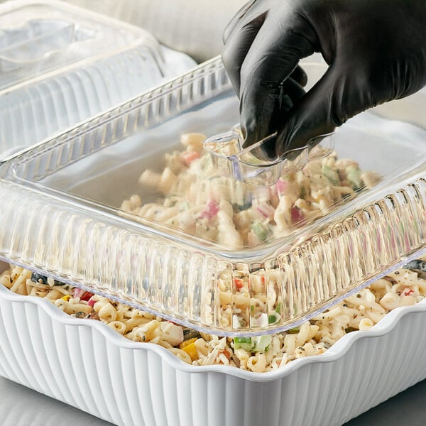 A person wearing black gloves putting food in a white deli crock.