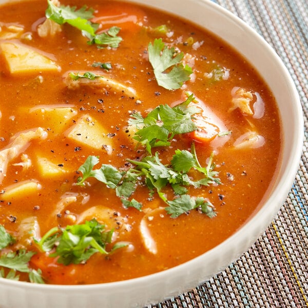 A bowl of Goya sofrito tomato soup with vegetables and spices on a white background.
