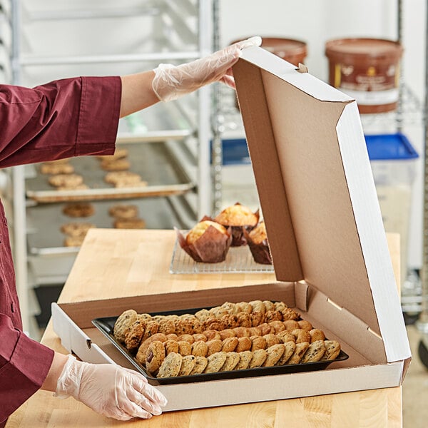 A person holding a white corrugated bakery box filled with pastries.