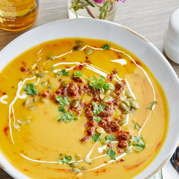 A bowl of soup with herbs and spices with a spoon on a table.