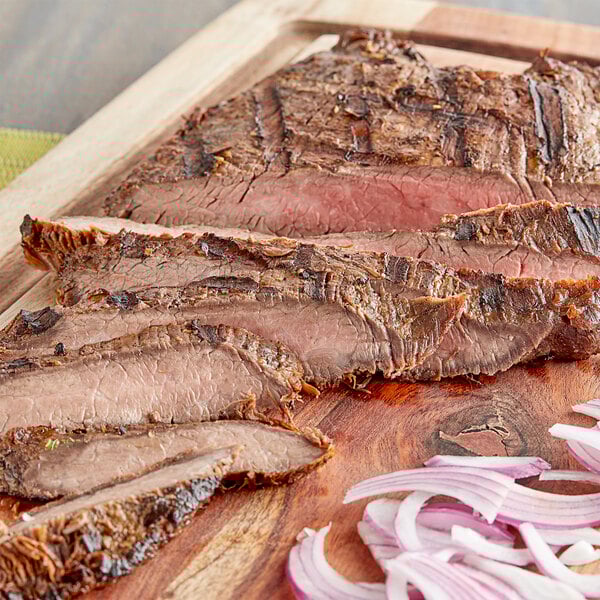 Sliced steak on a cutting board with onions.