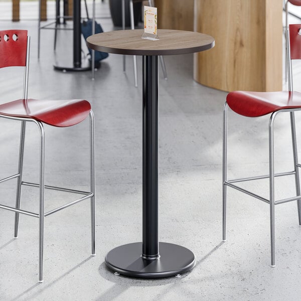 A round, 24-inch laminated table top with a reversible white birch and ash finish, mounted on a black pedestal base.