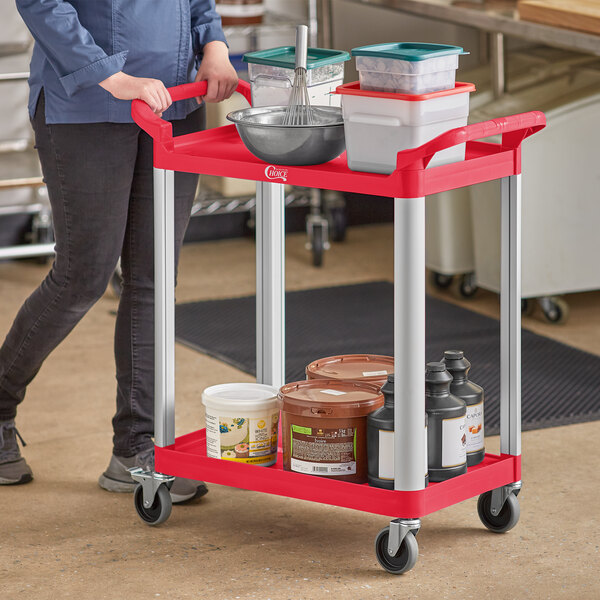 A woman pushing a red Choice utility cart with containers on it.