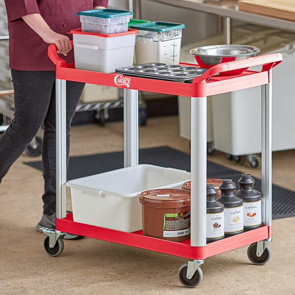 A woman pushing a red Choice utility cart with food containers.