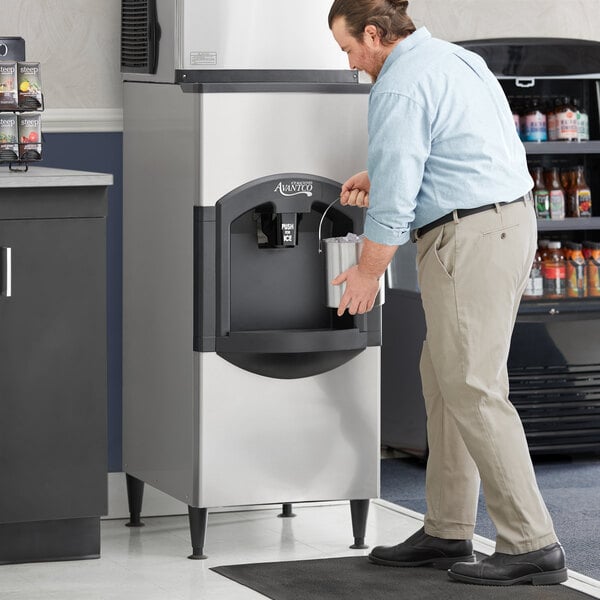 A person holding a bucket of ice next to an Avantco hotel ice dispenser.